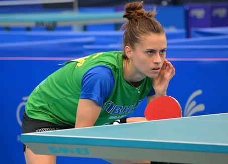 atleta de tênis de mesa feminino agachada em frente a mesa
