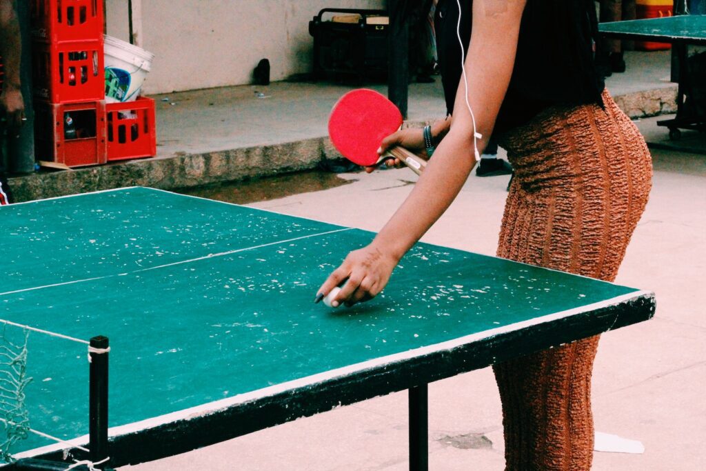 woman in brown tank top holding red and black table tennis racket
